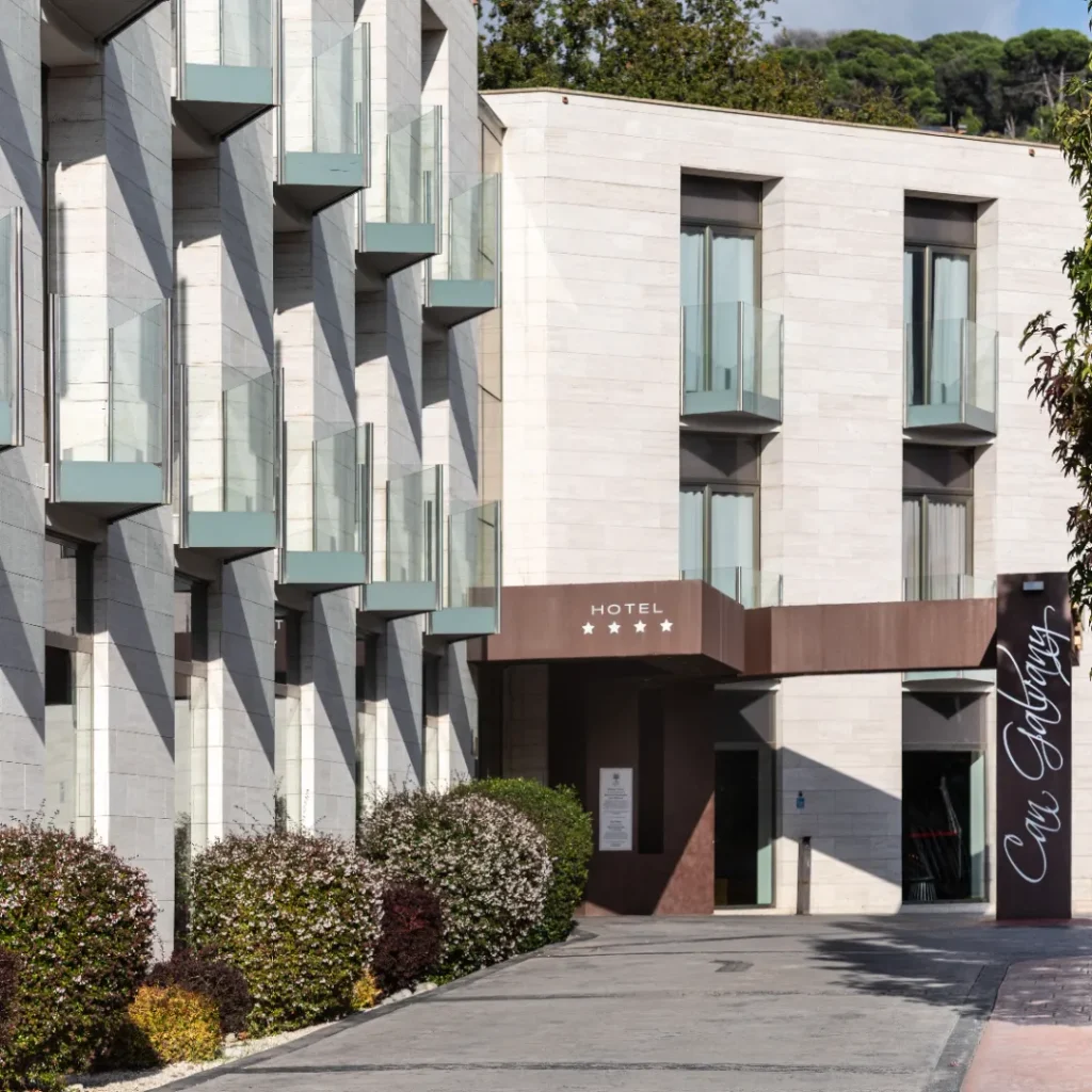 Entrada de un hotel con un camino peatonal flanqueado por árboles verdes.