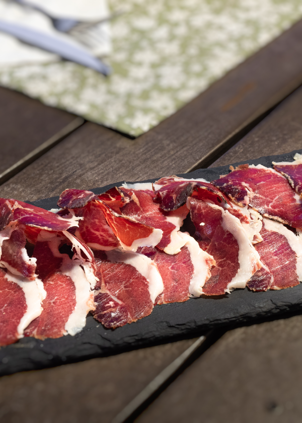 Un plato de carne sobre una pizarra negra, acompañado de un cuchillo y un tenedor.