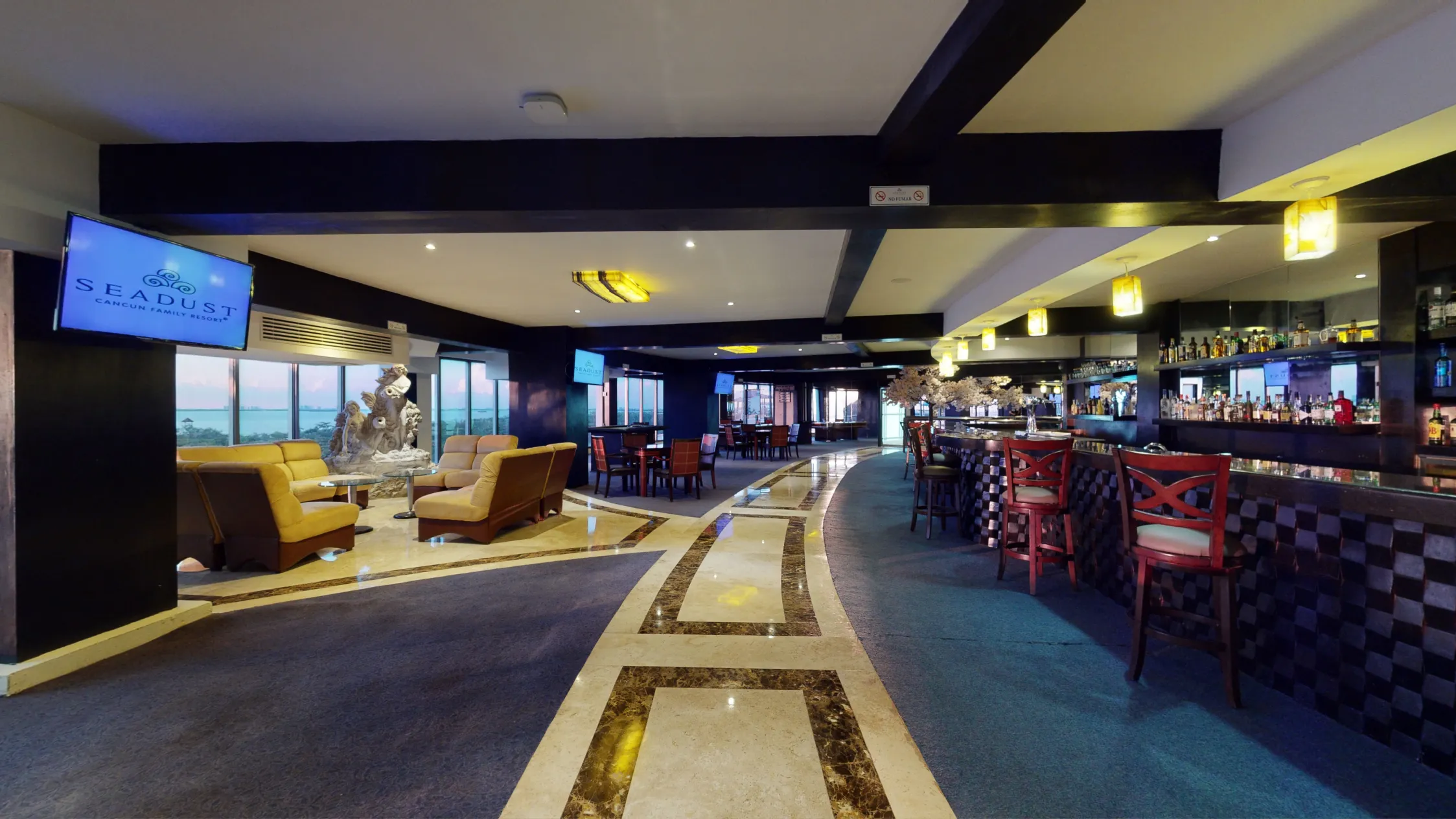 Hotel bar lounge with seating, decorative floor, and ambient lighting. A sculpture and TV screen are visible.