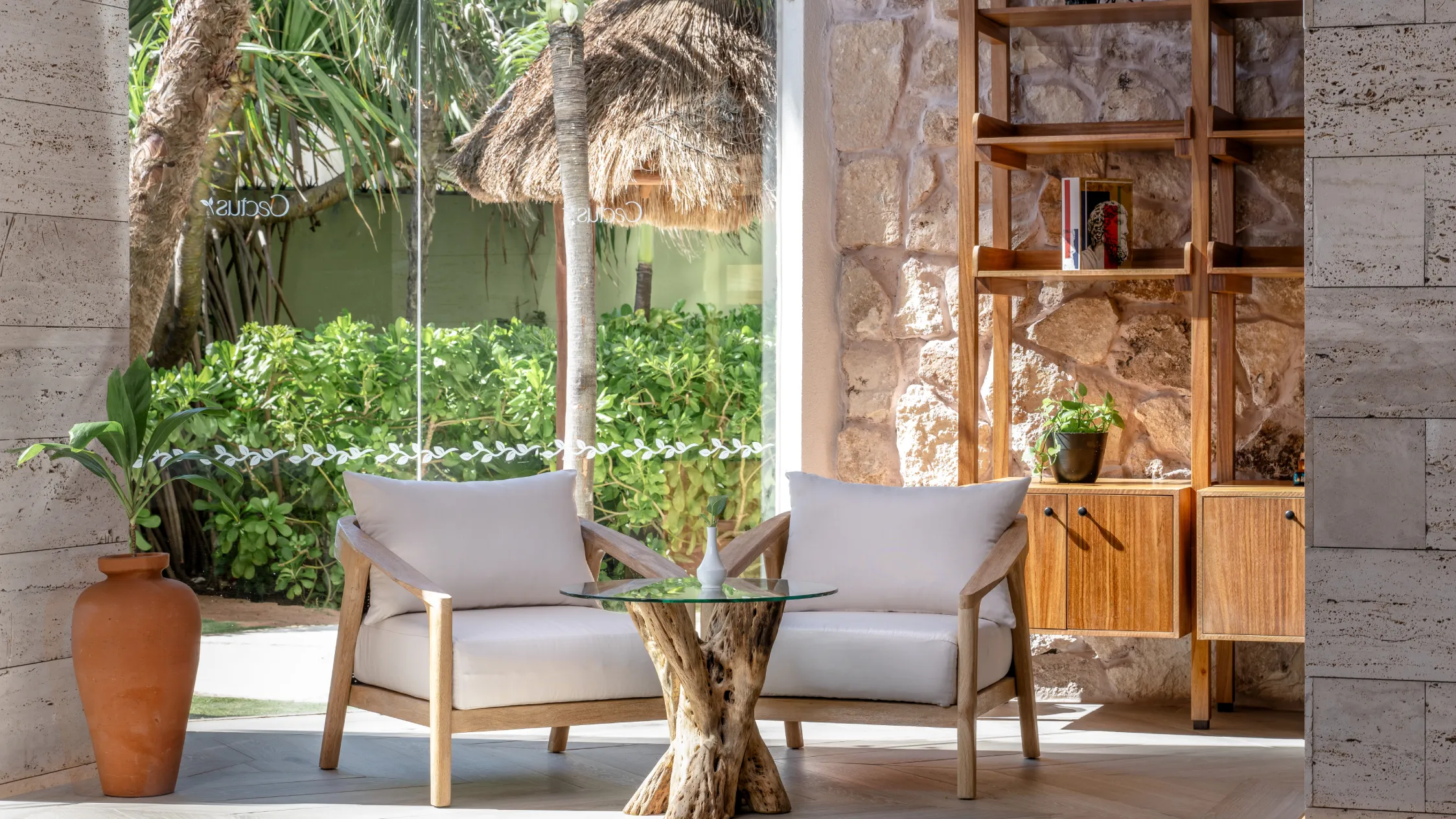 Cozy seating with white chairs and a glass table, surrounded by plants and stone walls.