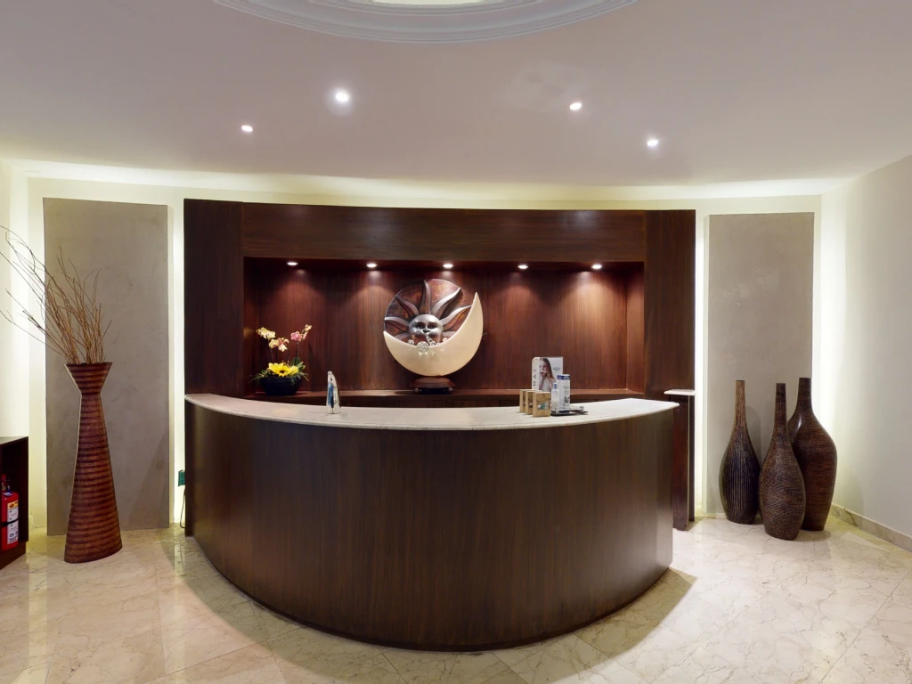 A modern, dimly lit reception desk with decorative vases and a large wall sculpture in a minimalist lobby setting.