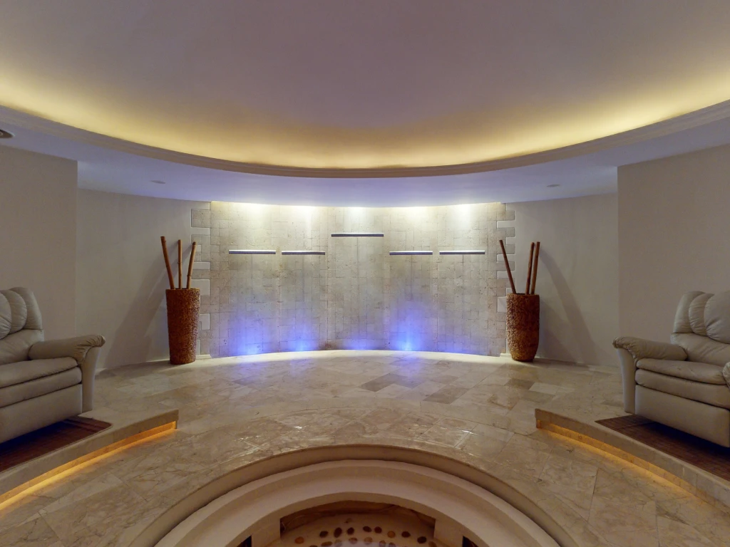 Spacious room with stone wall, blue lighting, two beige sofas, and decorative vases on each side.