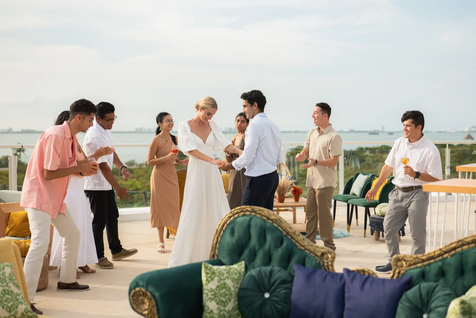 A joyful outdoor gathering with people dancing and holding drinks on a terrace overlooking a scenic view.