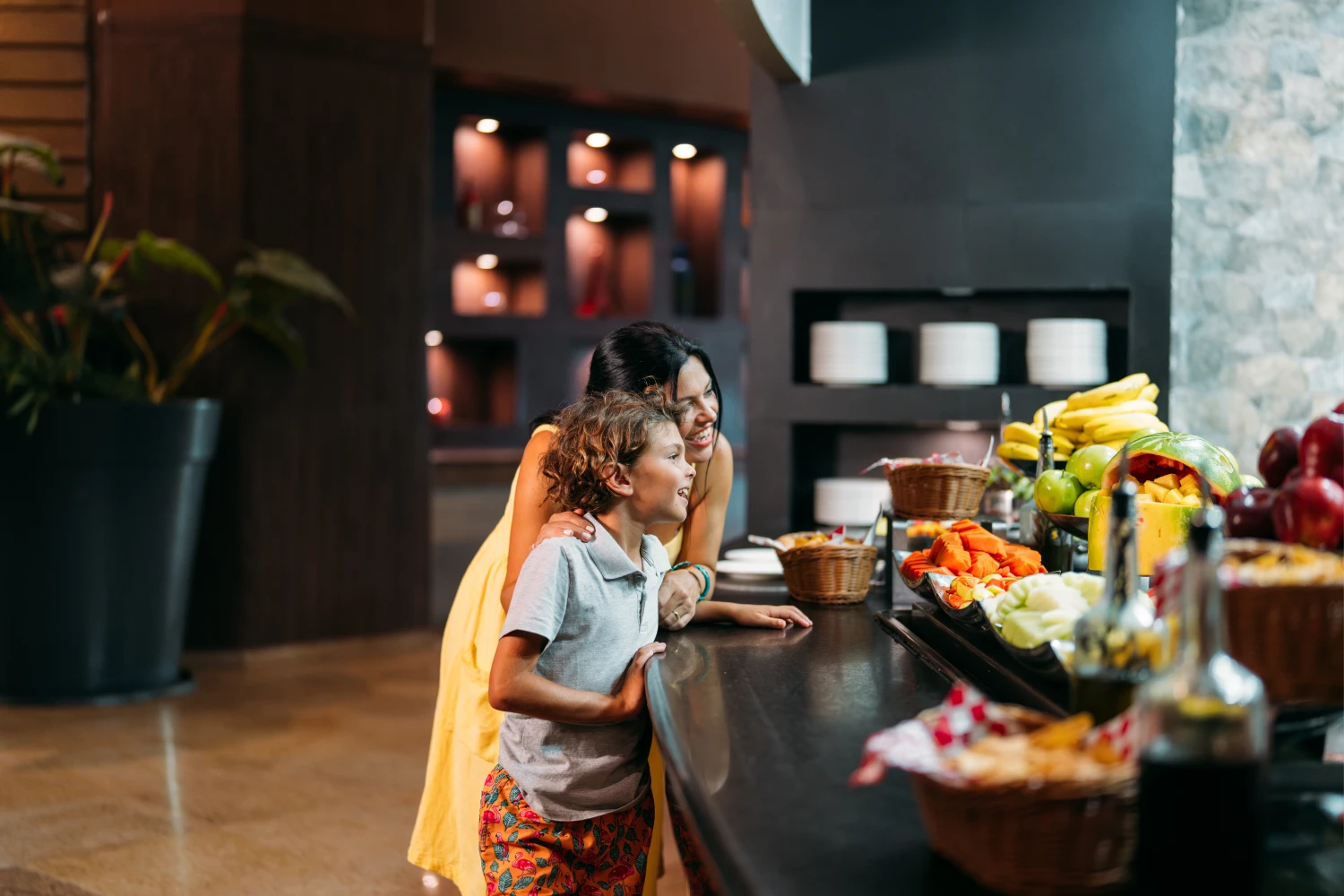 Child and woman smiling at a colorful fruit buffet in a restaurant setting.
