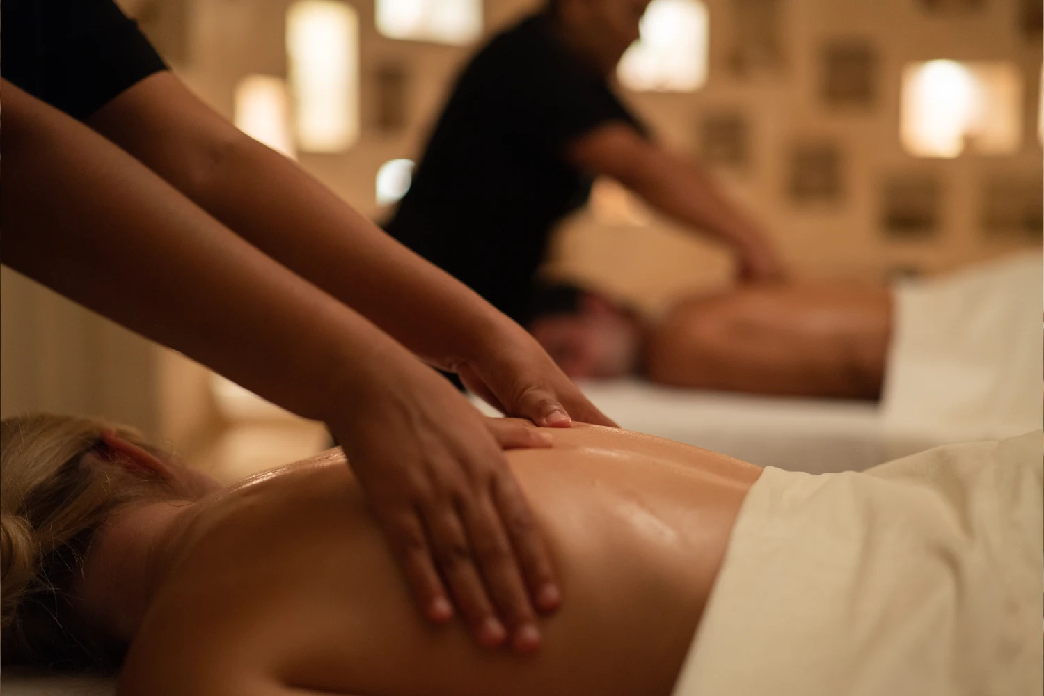 Two people receiving a back massage in a tranquil spa setting, with focus on hands applying oil.