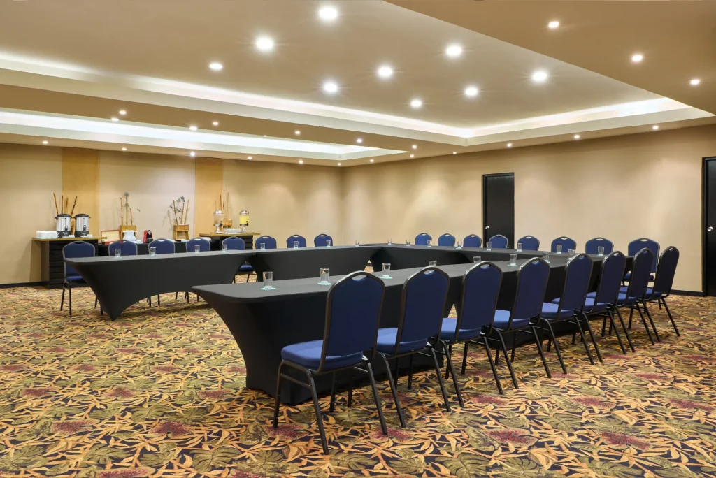 Conference room with U-shaped table setup, blue chairs, and refreshments in the back.