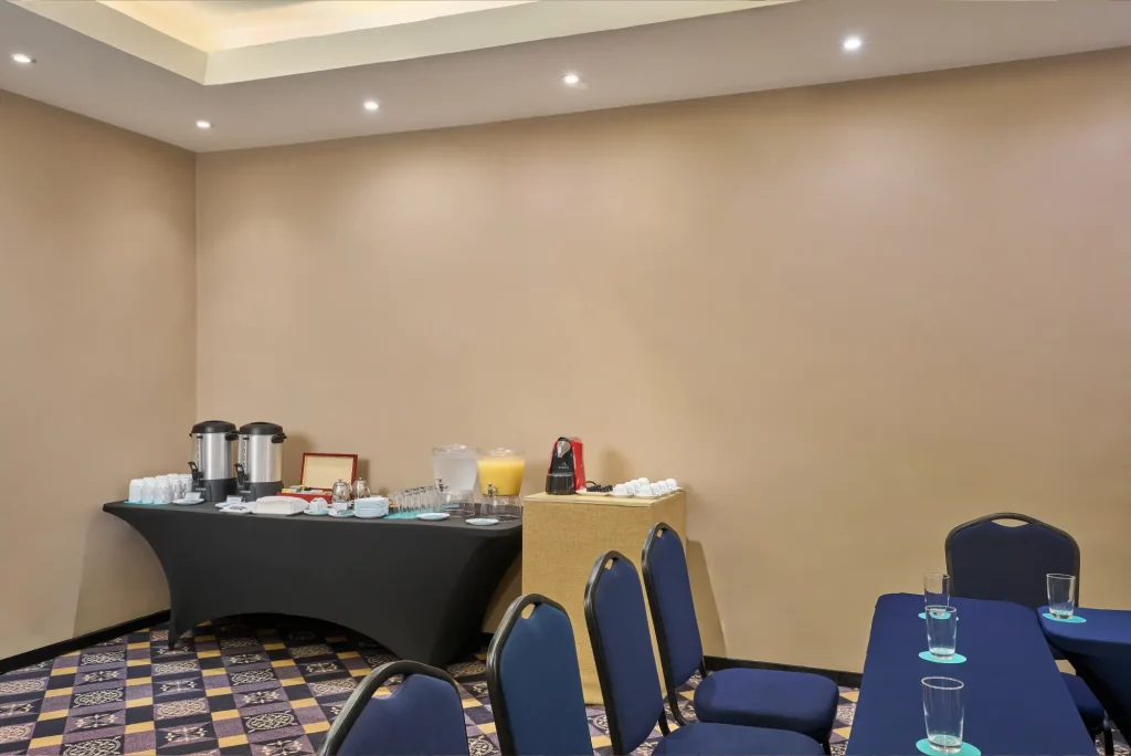 Room with a beverage station, blue chairs, and tables with glasses.