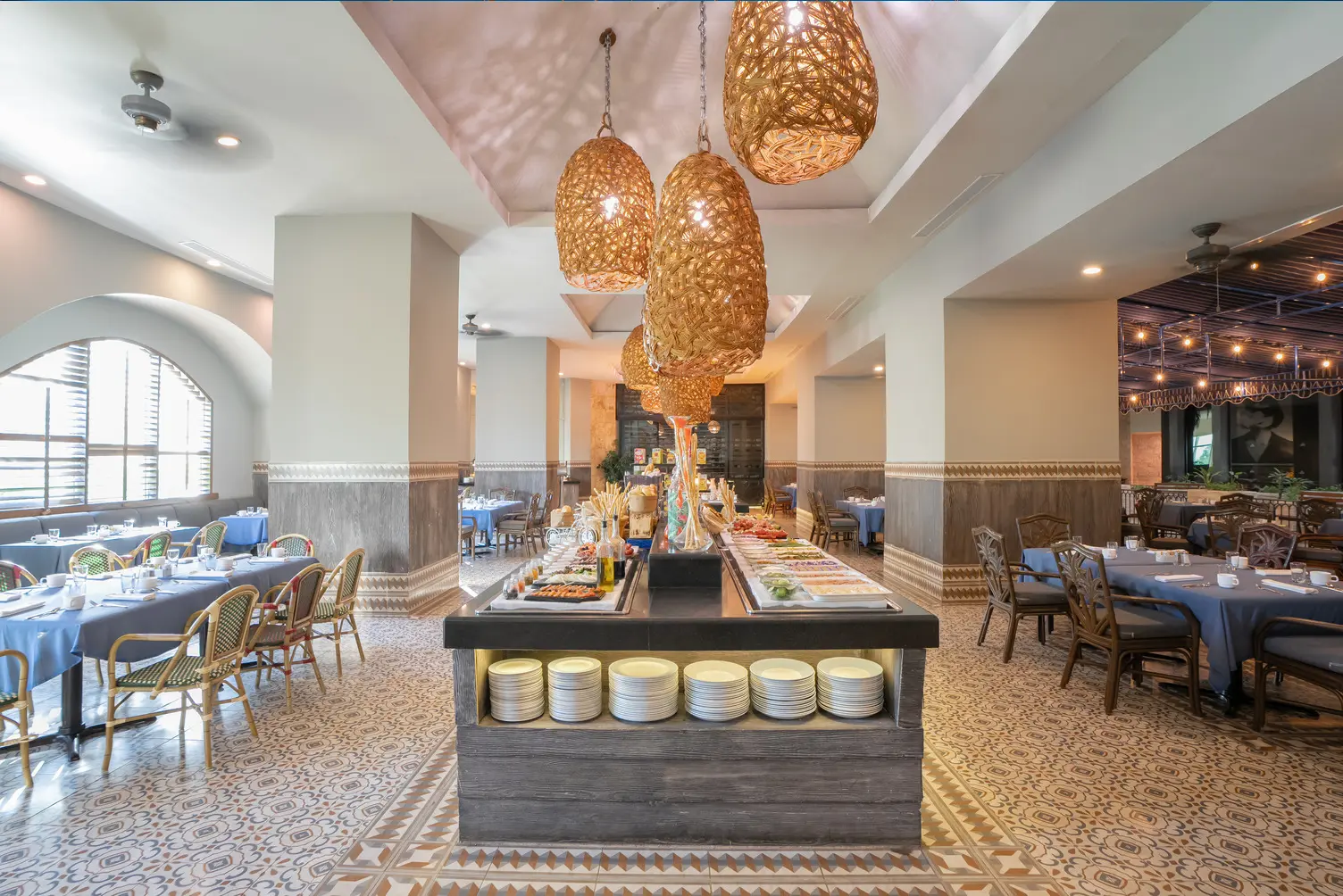 Spacious restaurant with decorative lights, buffet table in center, and tables covered with blue cloths.