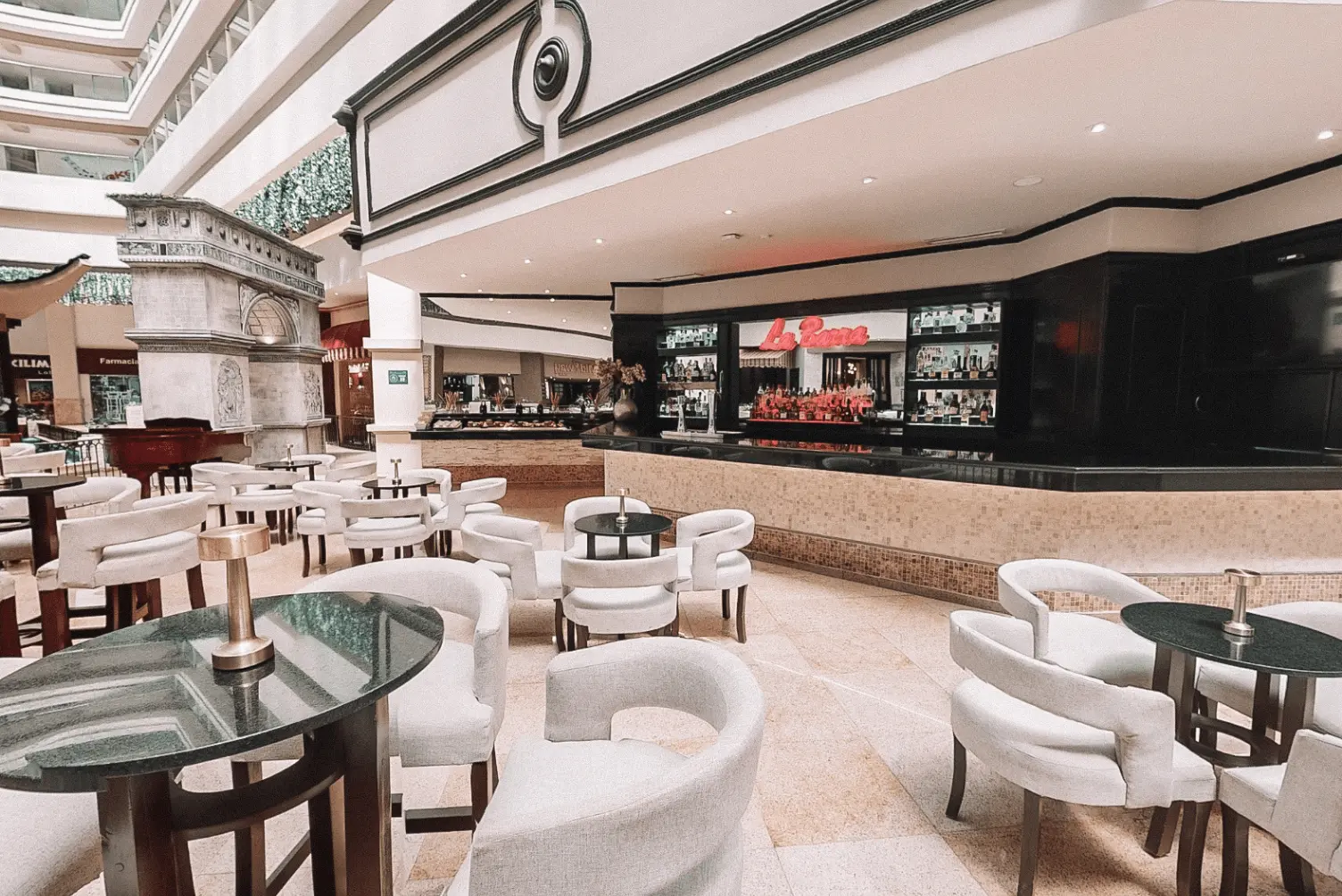 Modern bar and lounge area with white chairs and black tables, featuring a visible bar counter and shelves.