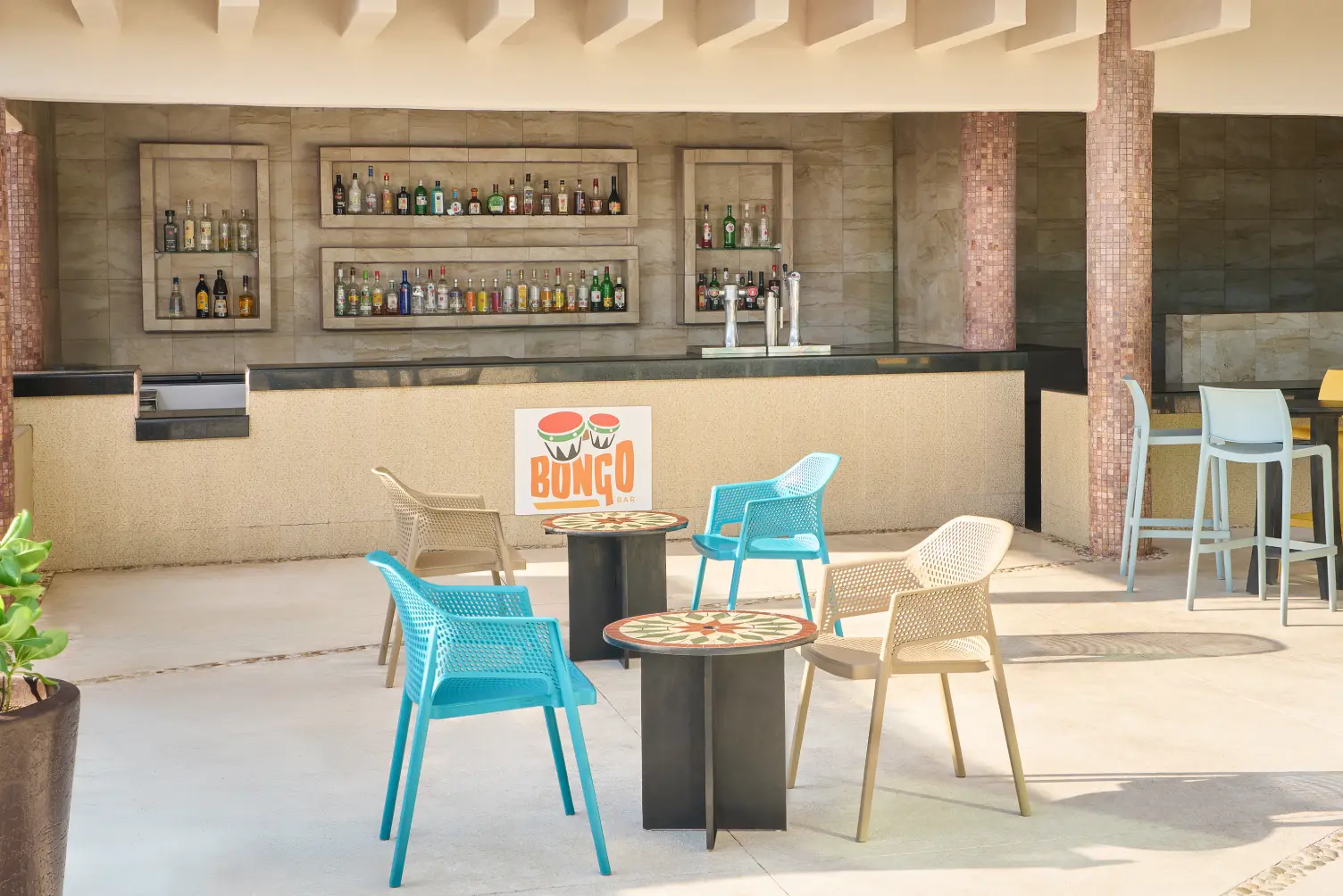 Open-air bar with colorful chairs and tables in front of a counter displaying various bottles and a "Bongo" sign.