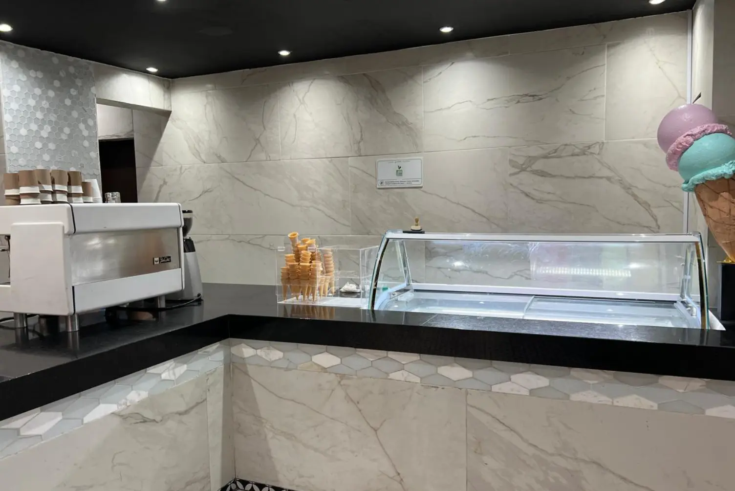 Empty ice cream shop counter with ice cream cone display and espresso machine.