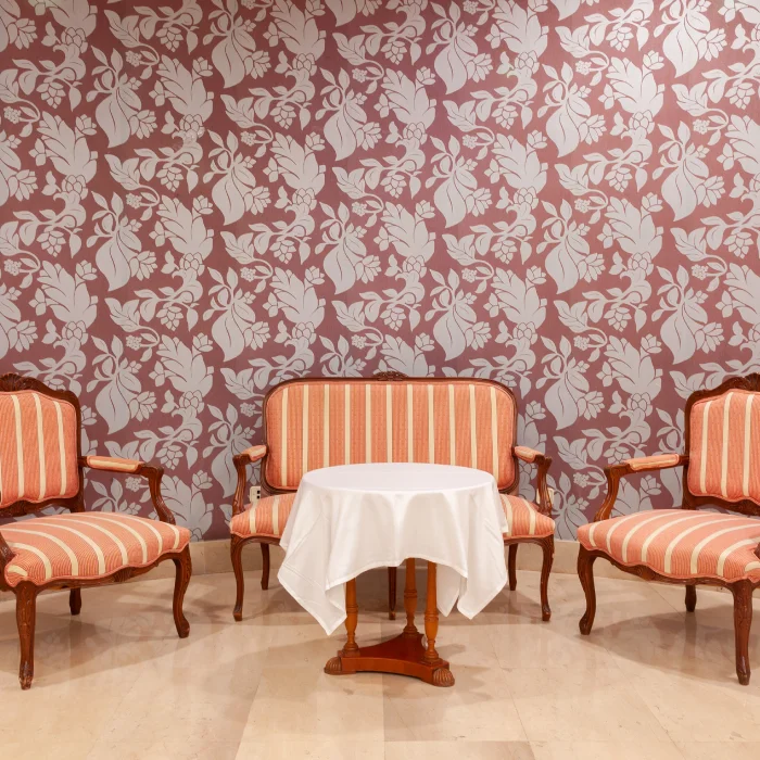 Sala con sofás y sillones de rayas rojas, mesa redonda con mantel blanco y fondo de papel tapiz floral.