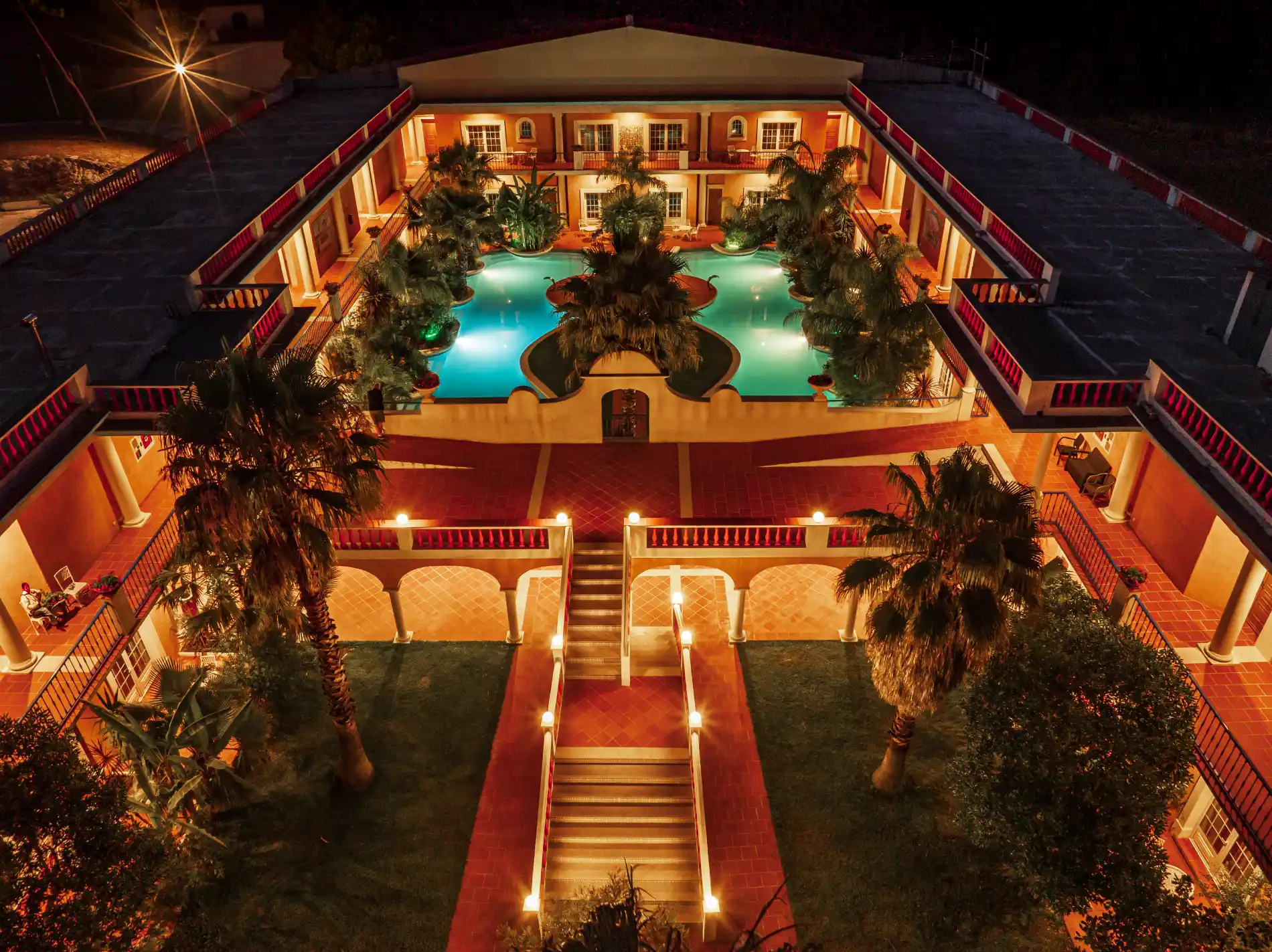 Lit courtyard with central pool and palm trees at night.