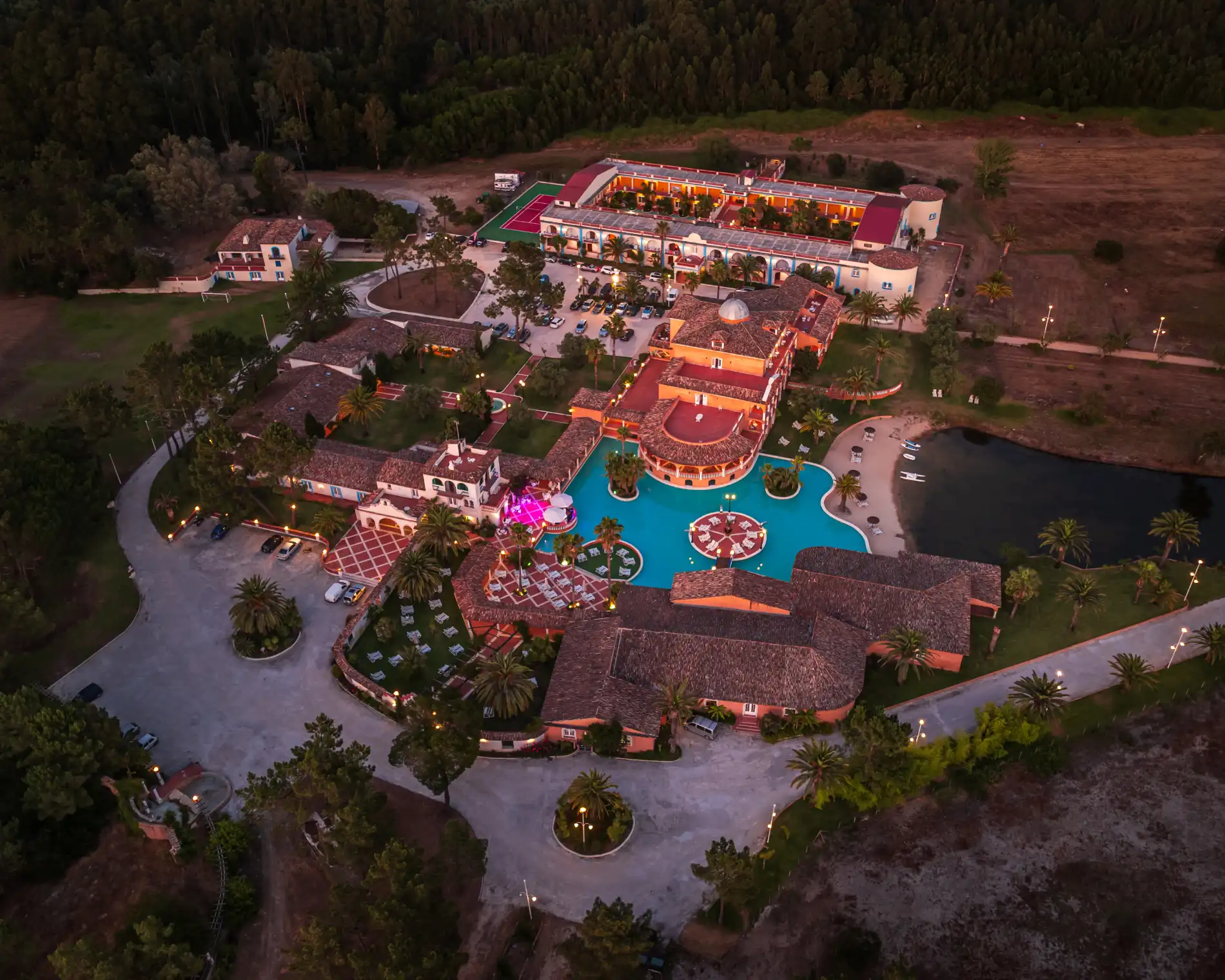 Aerial view of a vibrant hotel resort at sunset with a pool and gardens.