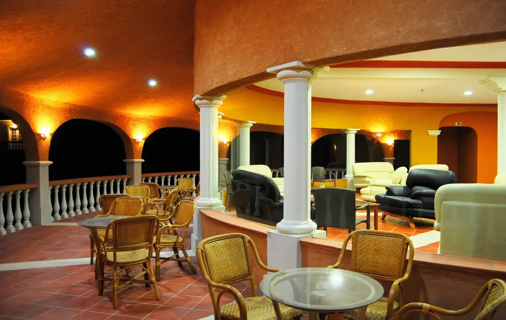 Elegant, open-air lounge with wicker chairs, tables, and cushioned seating under warm, ambient lighting.