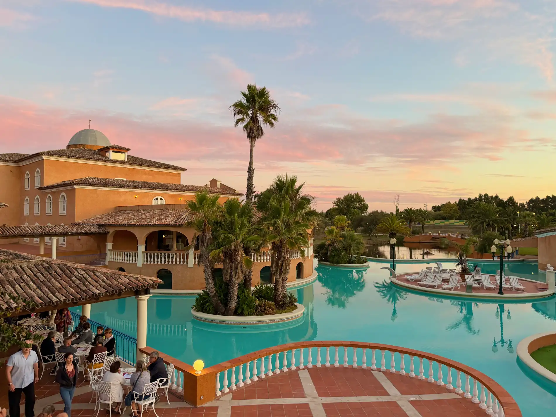 Poolside resort with palm trees and sunset sky.