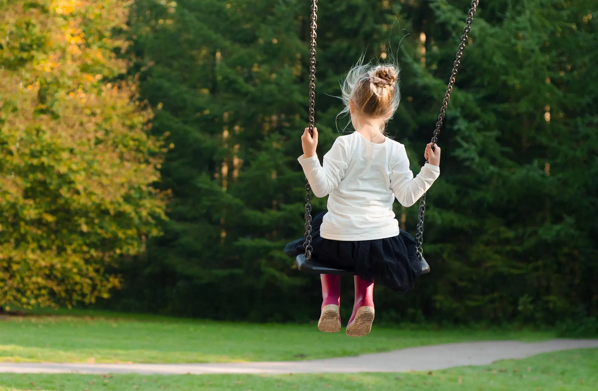Girl on a swing in a park with trees in the background.