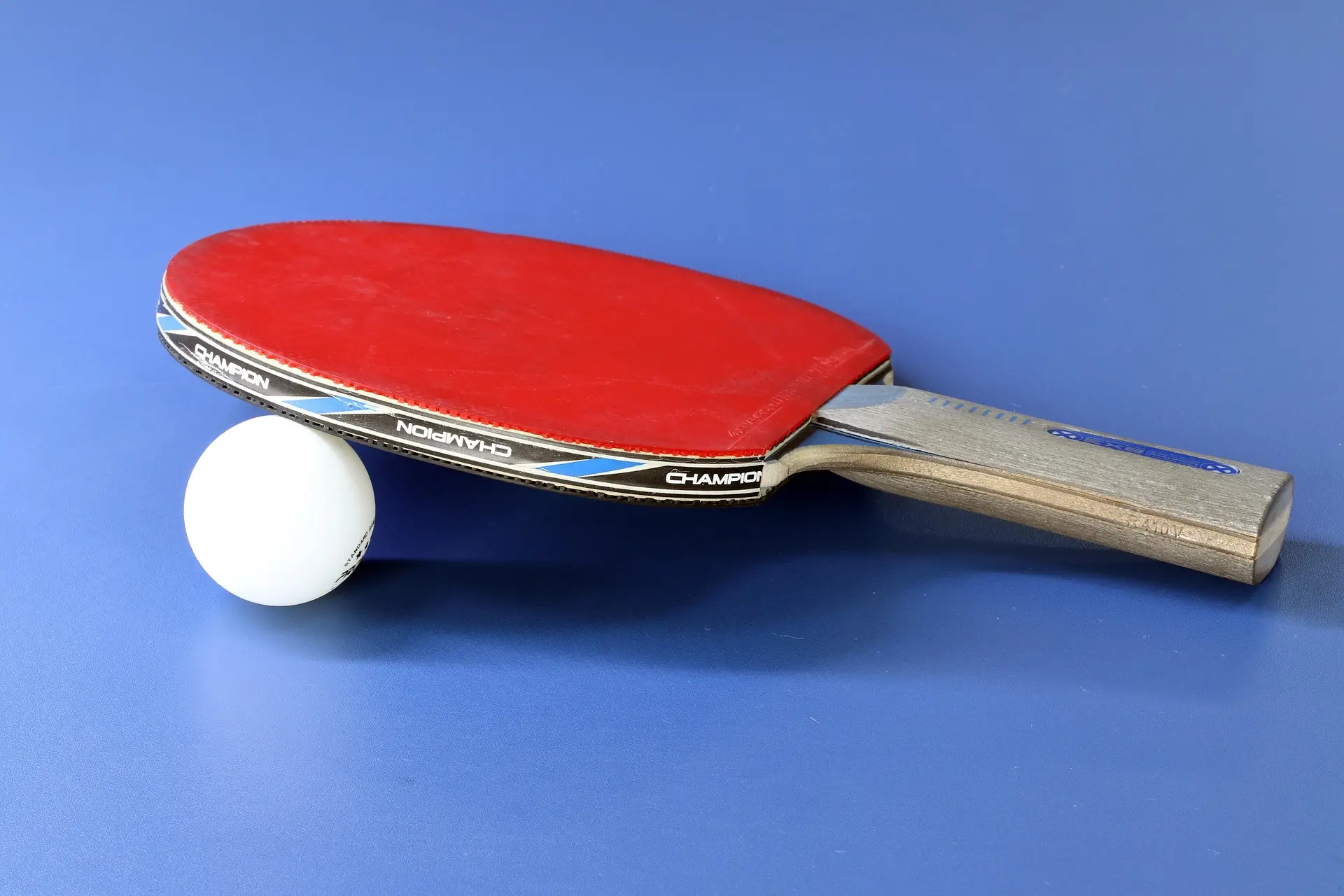Ping pong paddle and ball on a blue surface.