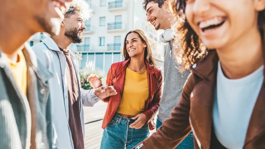 Grupo de amigos jóvenes riendo al aire libre en una ciudad, cerca de un edificio moderno.