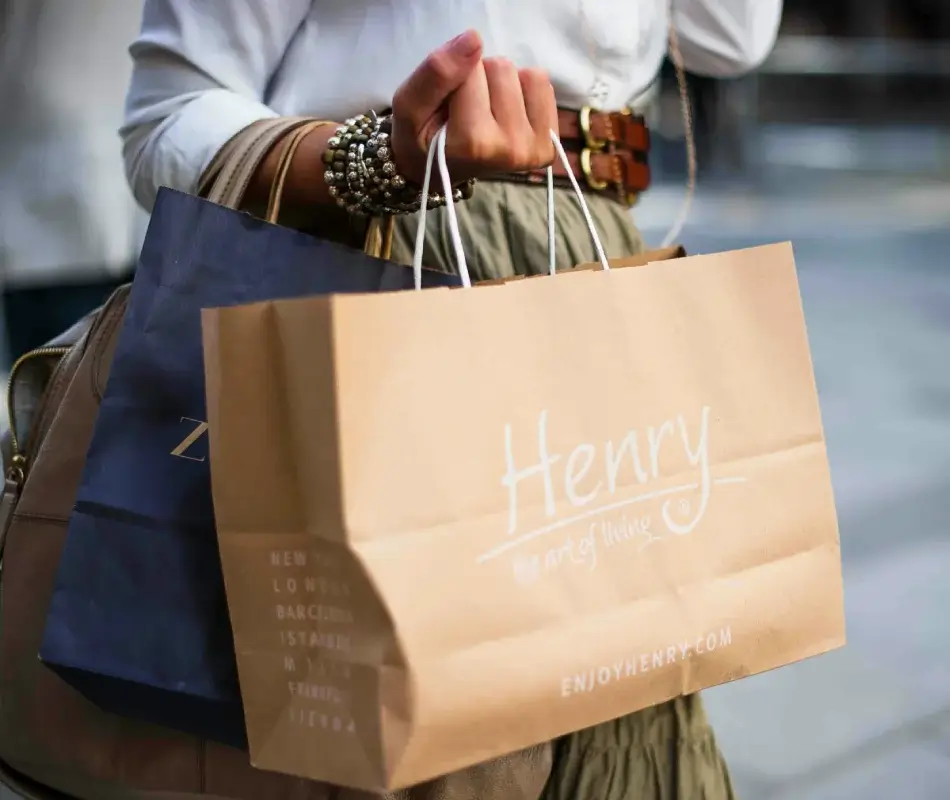 Persona sosteniendo bolsas de compras de papel con un brazalete en la muñeca.