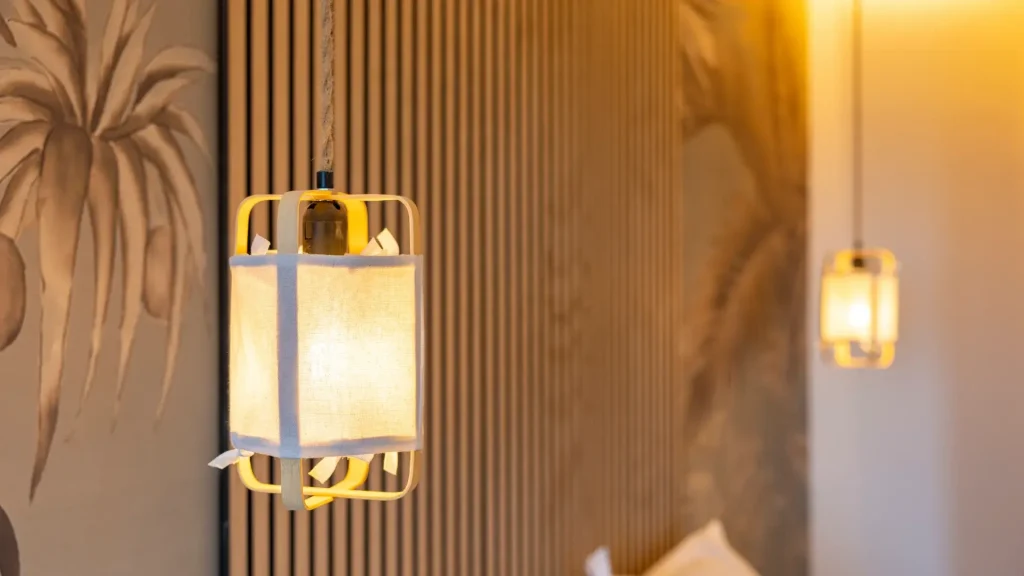 Lámpara colgante iluminada frente a un fondo con líneas verticales y diseño de palmeras difusas.