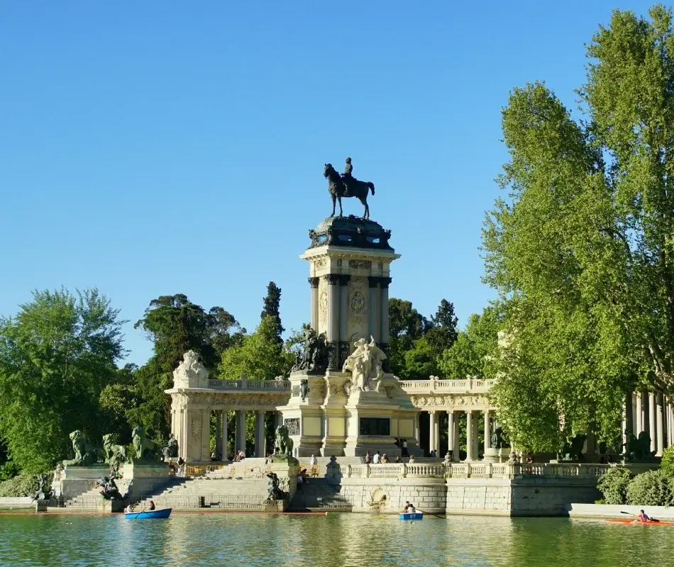 Monumento de equitación en estanque con árboles y cielo azul, gente paseando en bote.