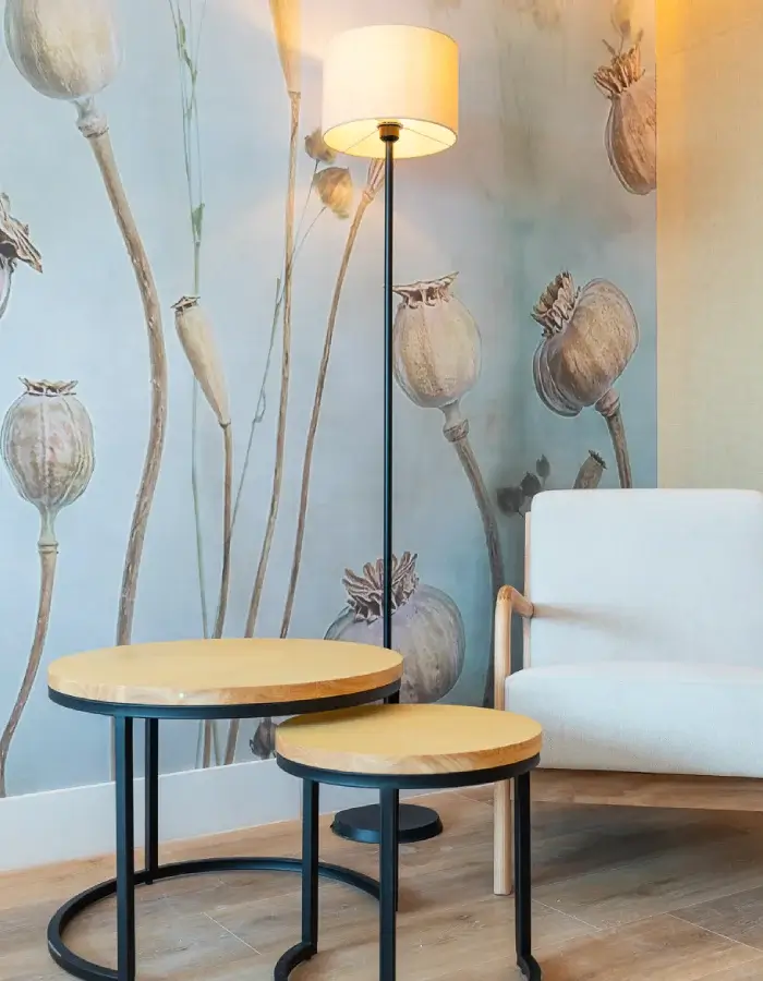 Sala moderna con lámpara de pie, silla blanca y mesas redondas frente a mural floral.