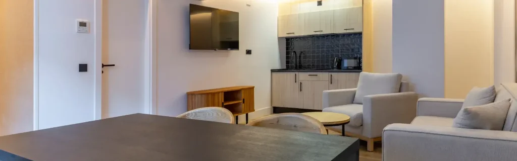 Sala moderna con sofá, TV, mesa, y cocina compacta en el fondo. Decoración minimalista.