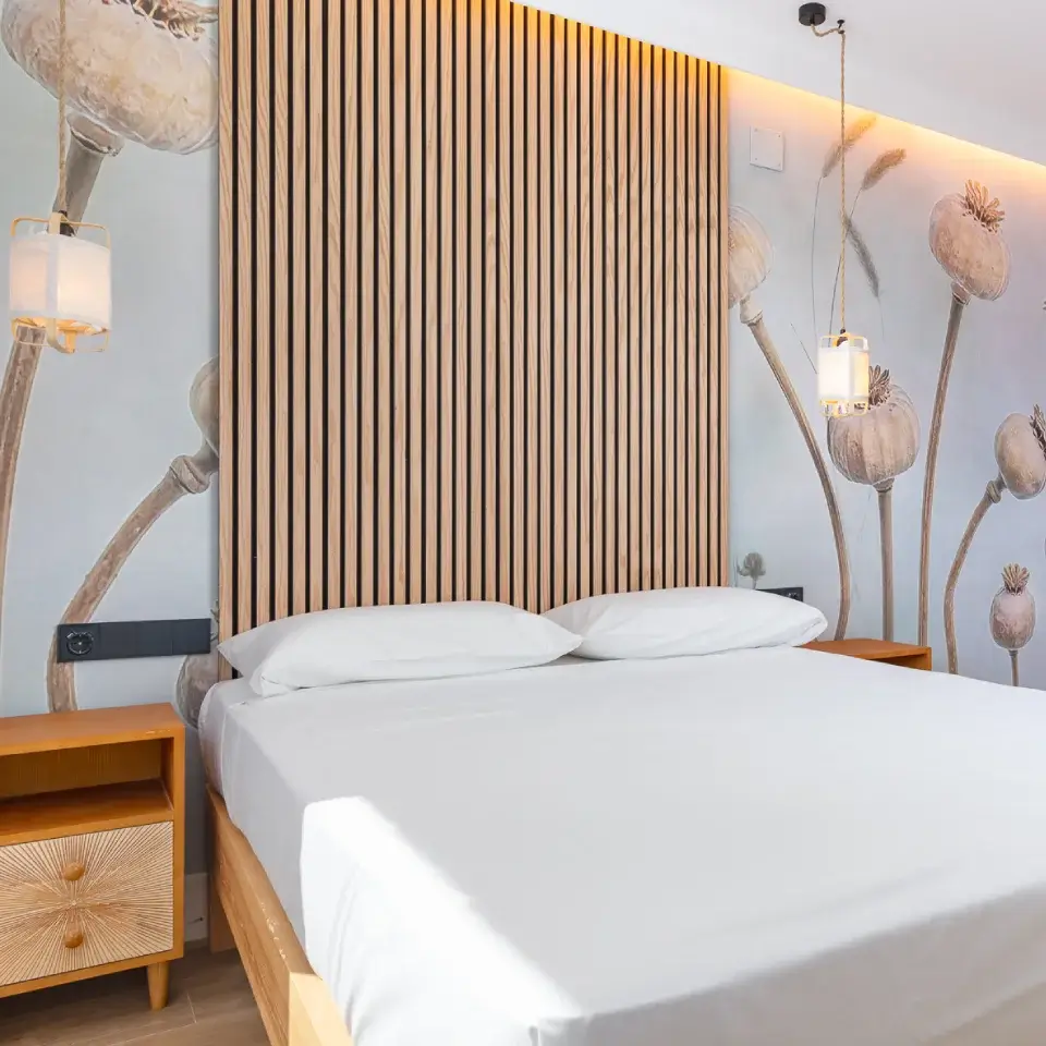 Habitación con cama doble, cabecero de madera y decoración de flores en la pared.