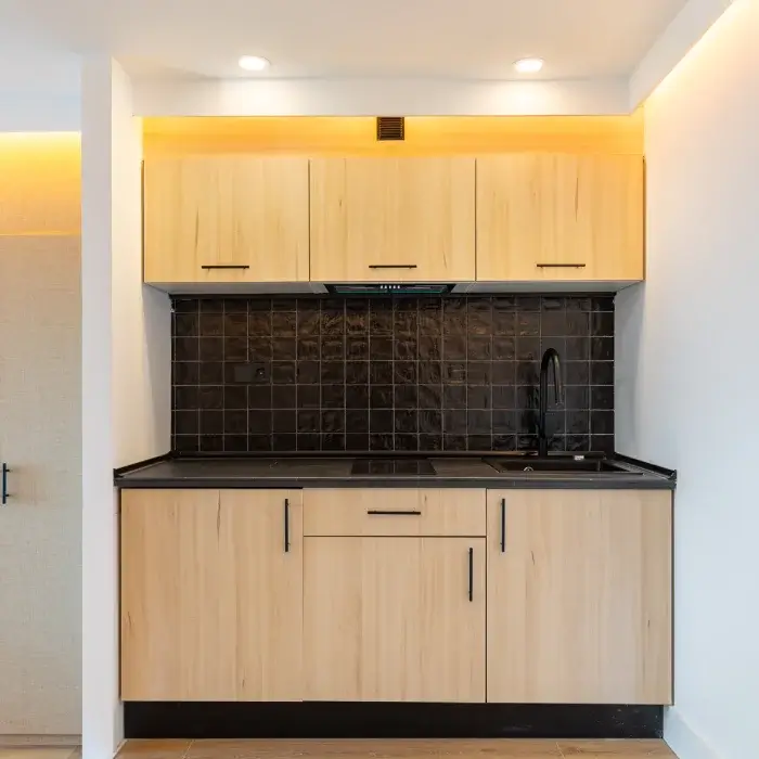 Cocina moderna con gabinetes de madera clara, azulejos negros y luces empotradas.