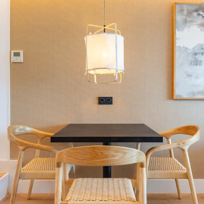 Mesa con lámpara colgante, tres sillas de madera y cuadro en pared. Decoración moderna.