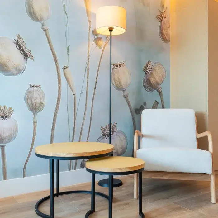 Sala moderna con lámpara, sillón blanco y mesas redondas, fondo de flores secas.