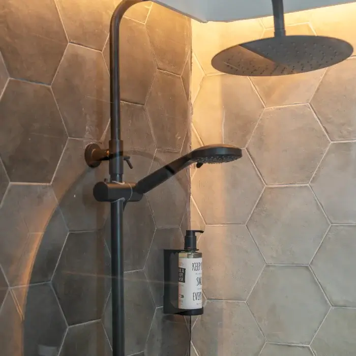 Ducha moderna con azulejos hexagonales grises y dispensador de jabón.