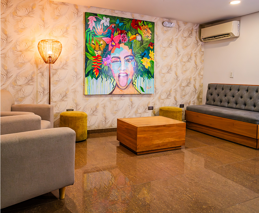 Sala de estar con tapizado claro, cuadro colorido en pared, lámpara de pie, mesa de madera y aire acondicionado.