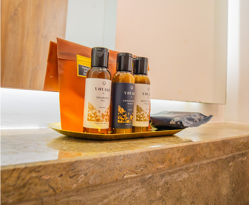 Set de amenidades: tres botellas de productos de cuidado personal y un paquete en una bandeja sobre un estante de mármol.