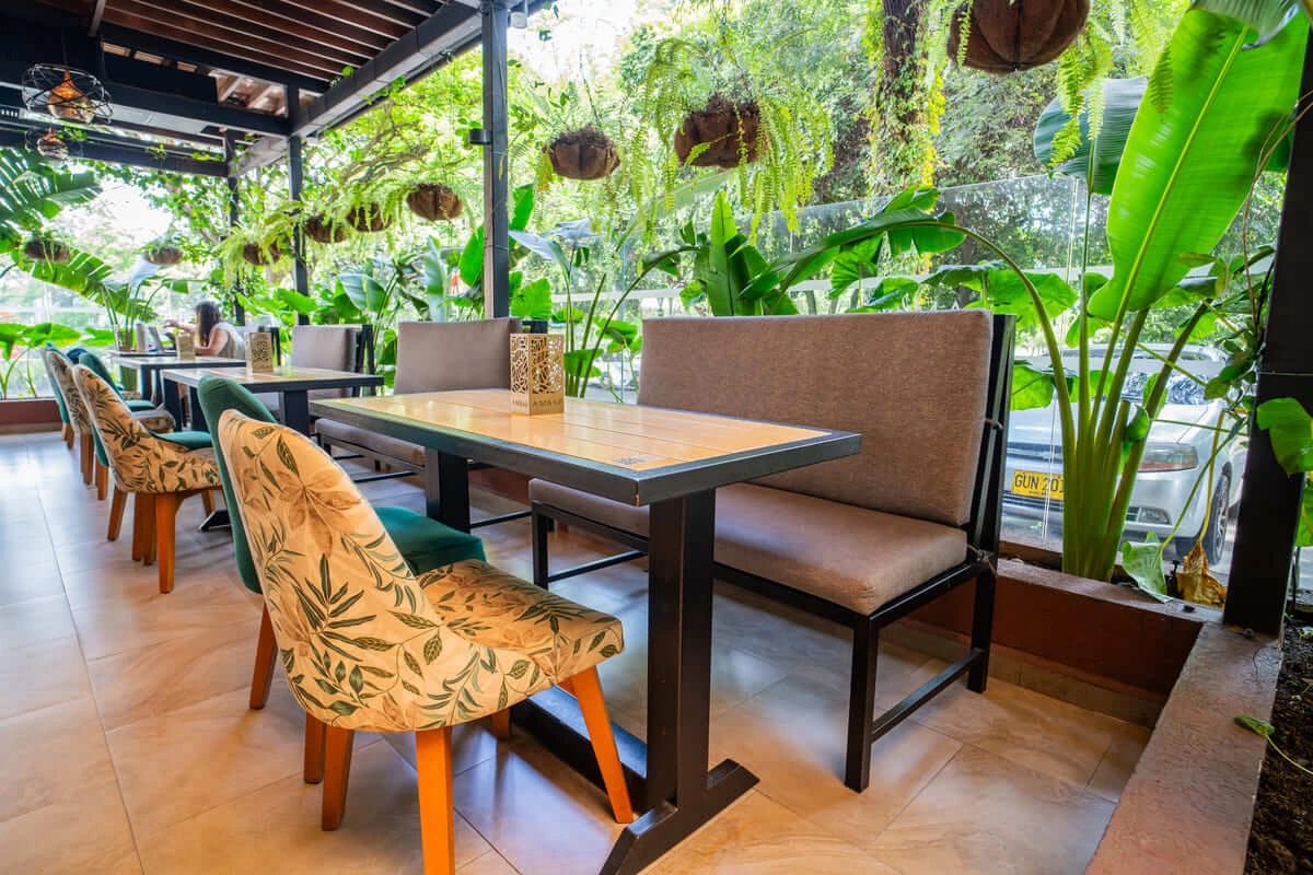 Terraza de restaurante con sillas decoradas, mesas de madera y plantas colgantes, vista hacia el exterior.