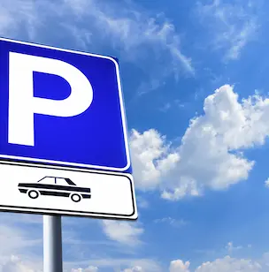 Panneau bleu de parking sous ciel bleu avec nuages blancs.