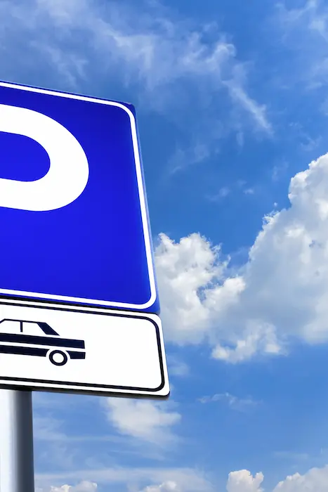 Panneau bleu de parking sous ciel bleu avec nuages blancs.