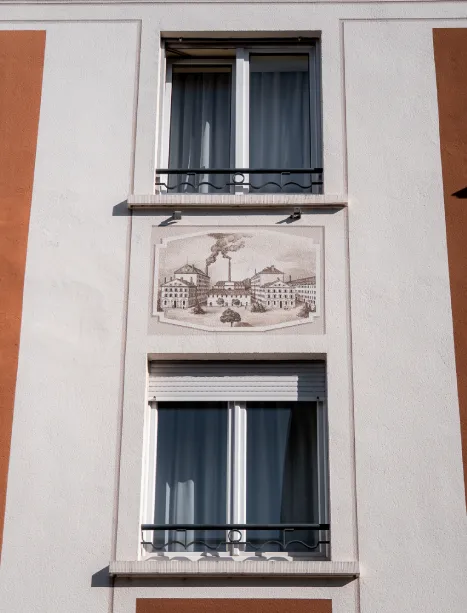 Façade avec fresque de bâtiment historique entre deux fenêtres à volets roulants.