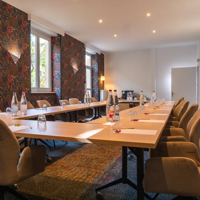 Salle de réunion élégante avec grande table en bois, chaises, bouteilles d'eau, papiers et verres placés pour réunion.