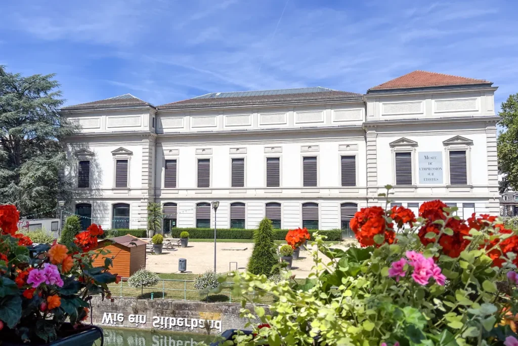 Bâtiment blanc avec jardin fleuri au premier plan, ciel bleu en arrière-plan.
