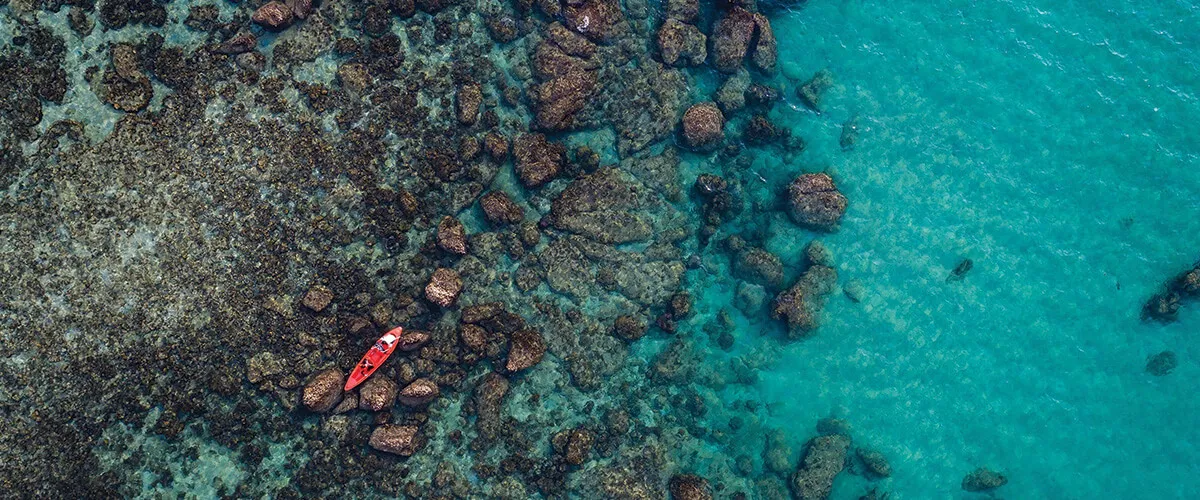 Vista a&eacute;rea de un kayak rojo entre rocas en aguas turquesas cristalinas.