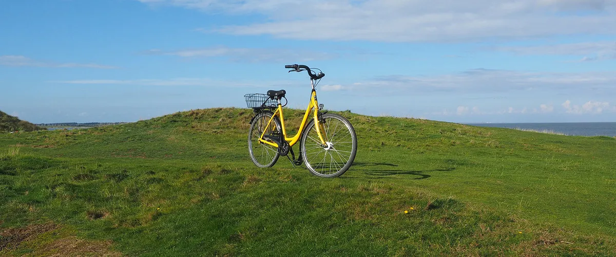 Bicicleta amarilla en una colina verde bajo un cielo azul parcialmente nublado, con el mar de fondo.