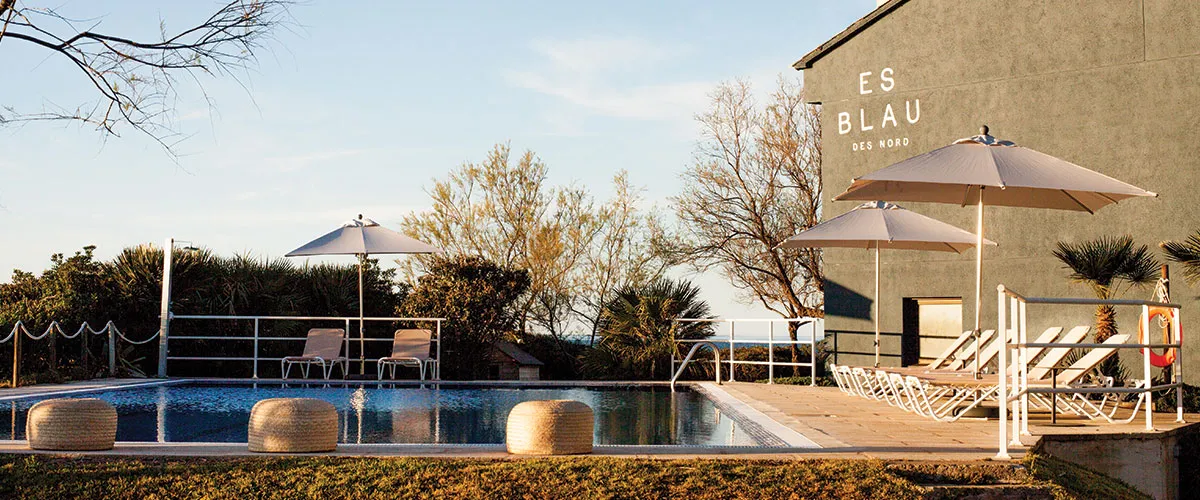 Piscina al aire libre con tumbonas y sombrillas junto a un edificio con el texto "ES BLAU DES NORD".