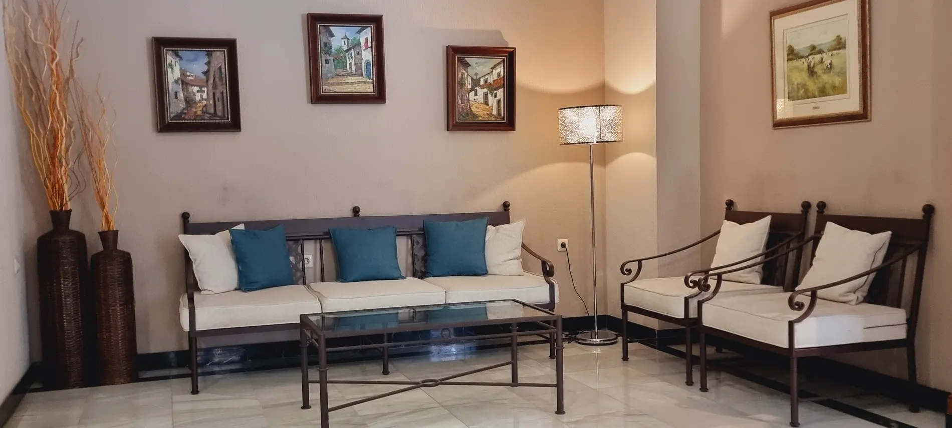 Sala con sofá y sillas de cojines blancos y azules, lámpara de pie, arte en la pared y adornos de jarrones altos.