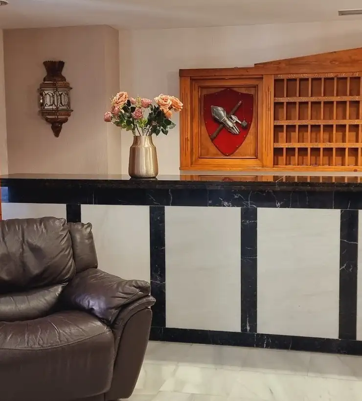 Recepción con mostrador de mármol negro, decoración de rosas en jarrón dorado y sillón de cuero oscuro.