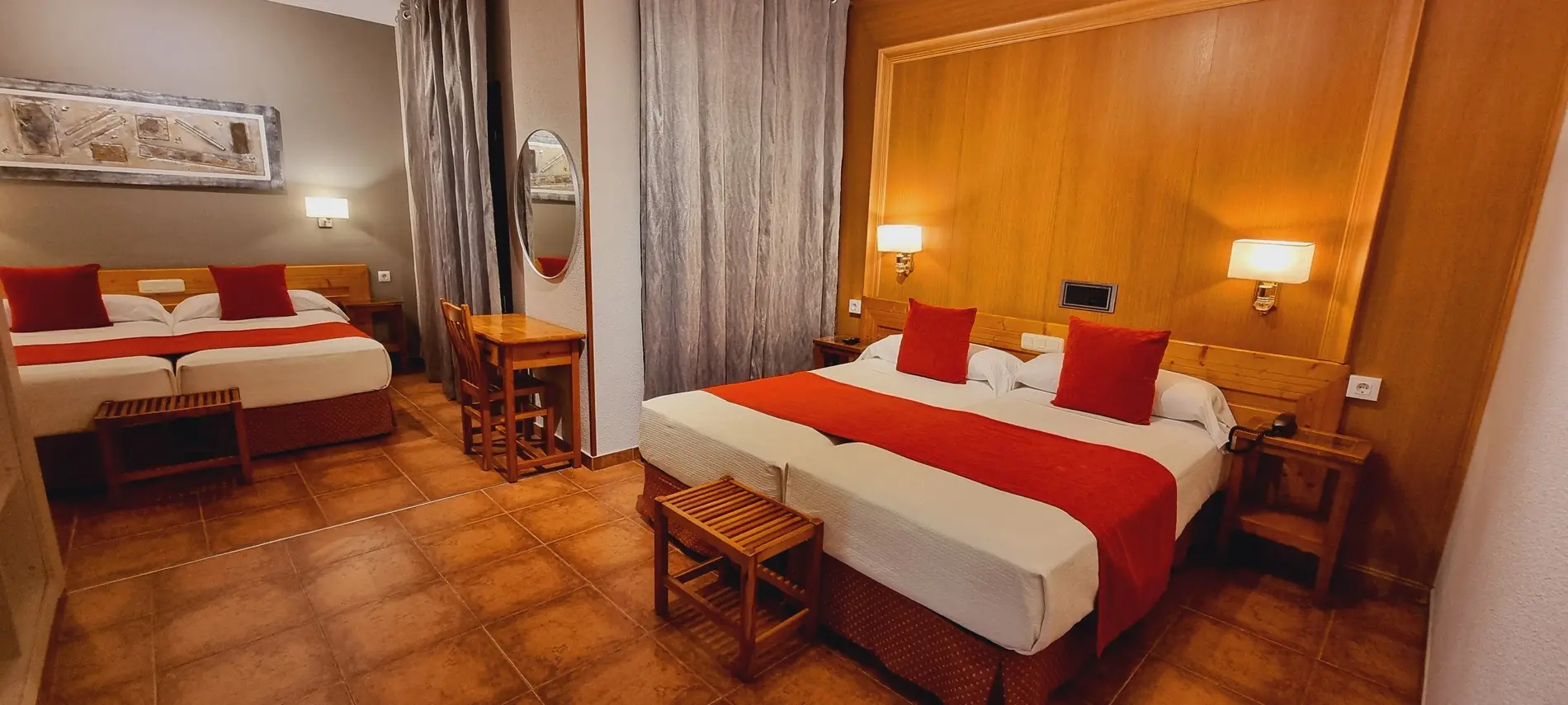 Habitación de hotel con dos camas matrimoniales, decoración en rojo y madera, mesas y lámparas de pared.