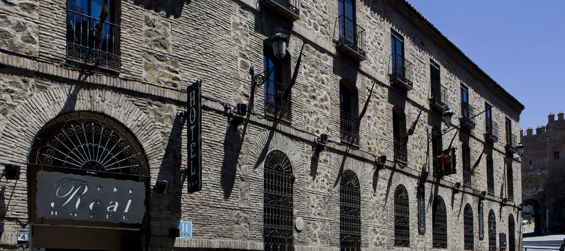 Fachada de un hotel antiguo con paredes de piedra, ventanas con rejas y un letrero que dice "Real Hotel".