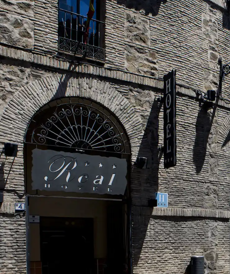 Fachada de un hotel de piedra con un letrero que dice "Real Hotel" y una señal vertical de "Hotel".