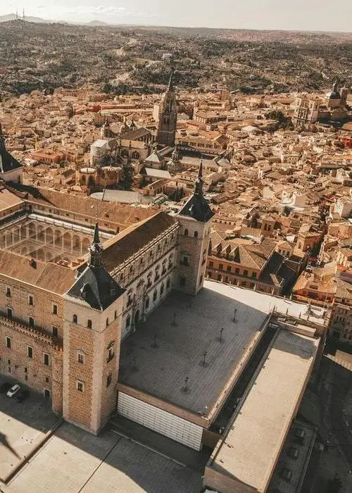 Vista aérea de una ciudad histórica con una gran catedral gótica y edificios antiguos de piedra bajo un cielo despejado.